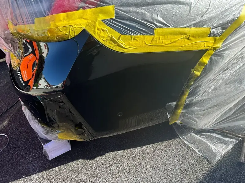 Freshly painted gloss black BMW rear bumper, still masked after spraying